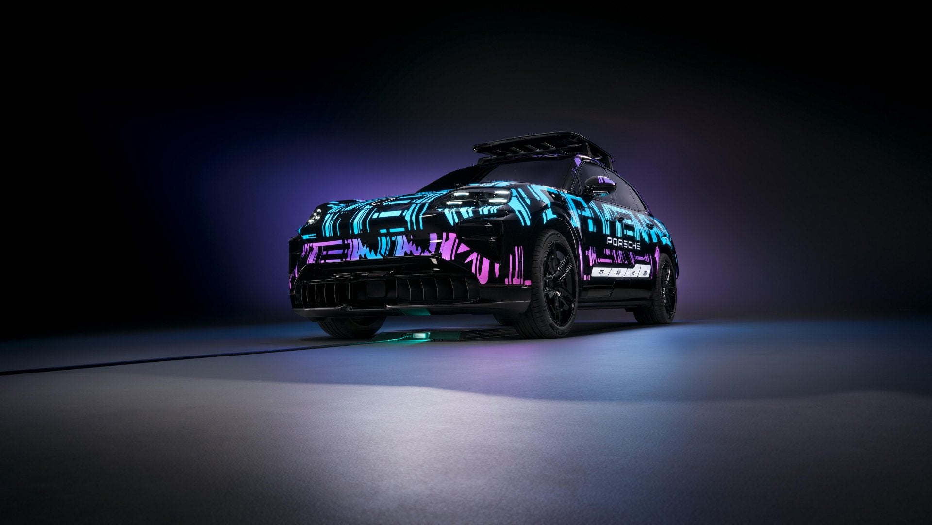 2026 Porsche Cayenne Turbo Electric prototype wrapped in neon test-livery under studio lighting with a wireless charging pad beneath it.