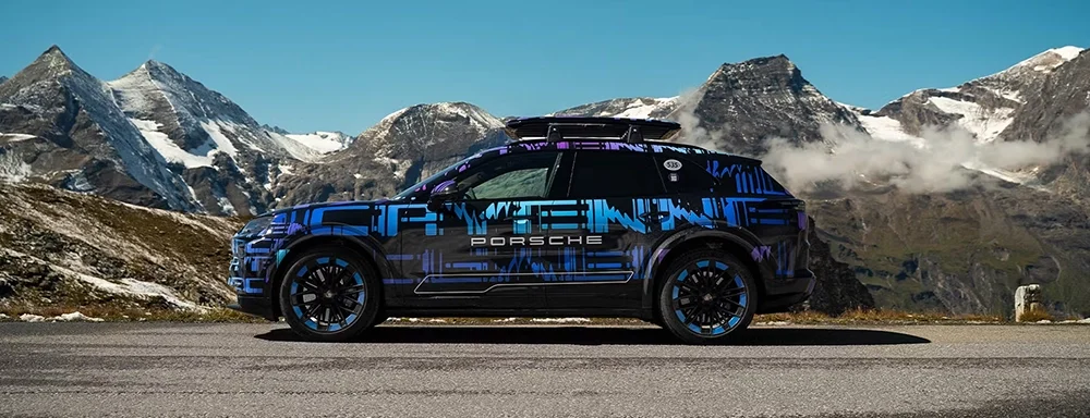 Side profile of a 2026 Porsche Cayenne Turbo Electric prototype in mountain terrain, highlighting its rugged stance and electric performance capability.